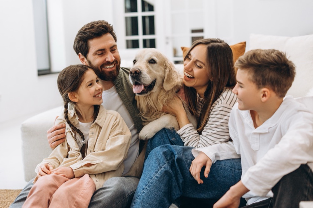 A family of four laughing on the sofa with their golden retriever