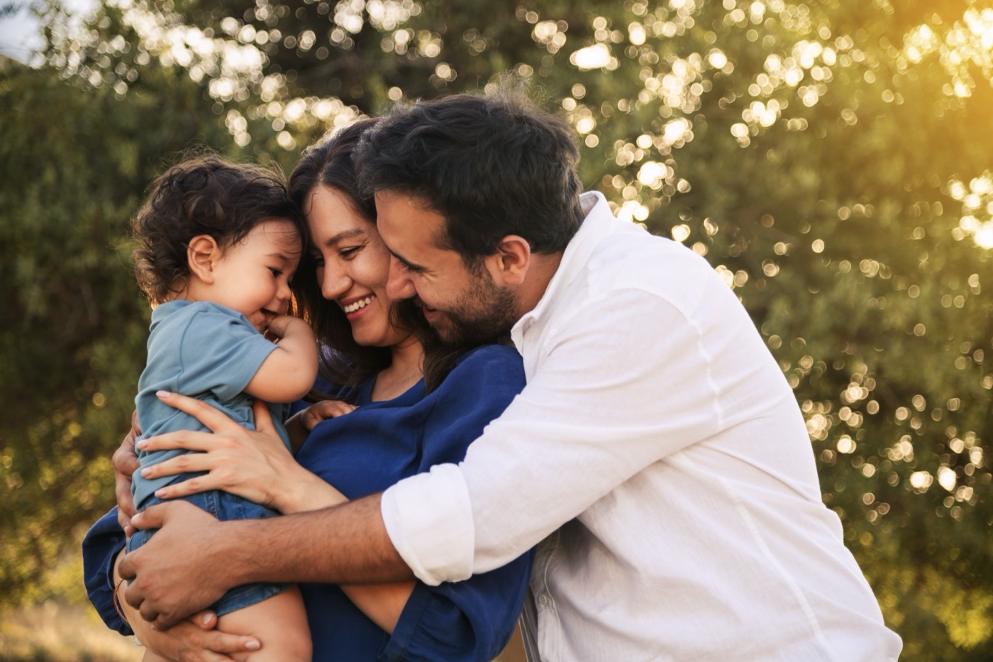 Parents hugging their toddler outdoors in golden light